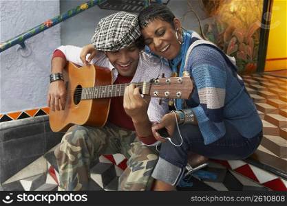 Young man playing a guitar and smiling with a young woman