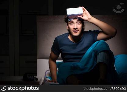 Young man playing computer games at night in bed
