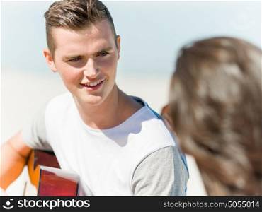 Young man playing guitar on beach. Picture of young smiling man playing guitar on beach