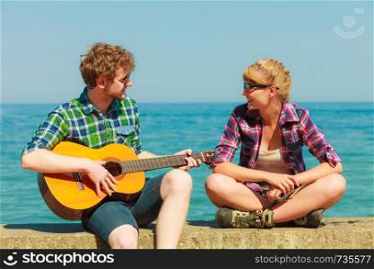 Young man playing guitar to his girlfriend outdoor by seaside - dating couple
