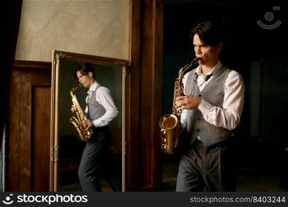 Young man playing saxophone in reflection of mirror at home. Young man playing saxophone at home