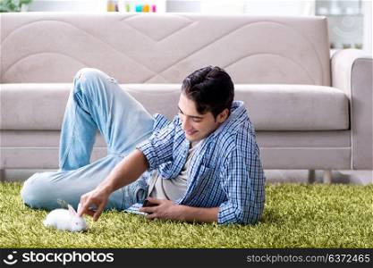 Young man playing with pet rabbit at home