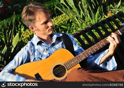 Young man plays guitar outside on a park bench