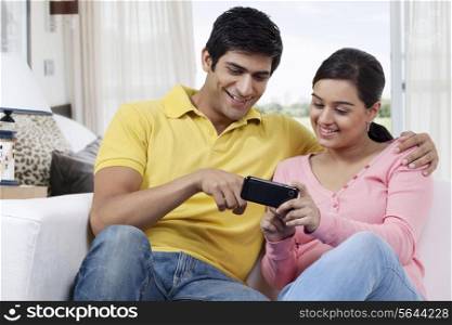 Young man pointing at mobile phone while watching something with girlfriend