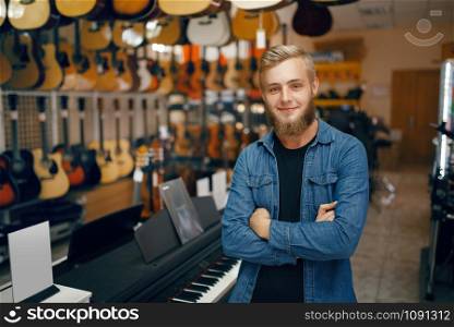 Young man poses at the showcase in music store. Assortment in musical instruments shop, musician buying equipment, music performer in market