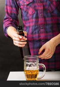 young man pouring beer from bottle into a mug glass