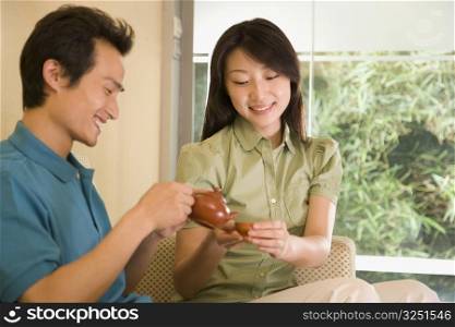 Young man pouring tea into a cup held by a young woman