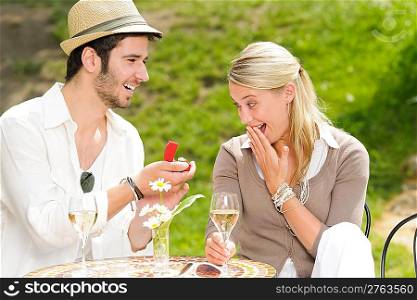 Young man proposing to girlfriend offering engagement ring sunny terrace