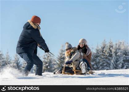 Young man pulling girls on winter sledge snow countryside