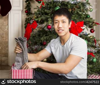Young man pulling out warm socks from gift bag with Christmas tree in background