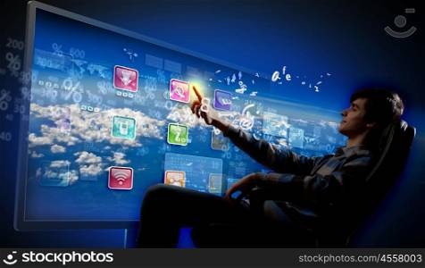 Young man pushing icon. Young man in armchair pushing icon on media screen