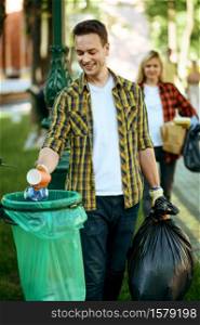 Young man puts garbage in plastic bag in park, volunteering. Male person cleans forest, ecological restoration, eco lifestyle, trash collection and recycling, ecology care, environment cleaning. Young man puts garbage in plastic bag in park