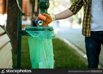 Young man puts garbage in plastic bag in park, volunteering. Male person cleans forest, ecological restoration, eco lifestyle, trash collection and recycling, ecology care, environment cleaning. Young man puts garbage in plastic bag in park