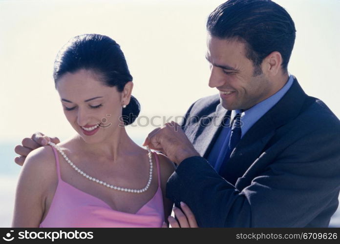 Young man putting a pearl necklace on a young woman