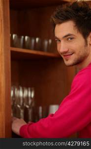 Young man putting glasses away in a cupboard