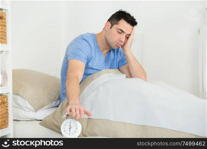 young man reaching for alarm in bed