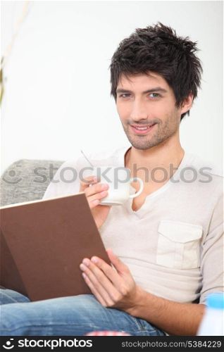 young man reading a book and drinking coffee on a couch