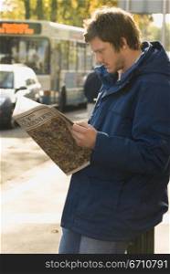Young man reading a magazine on a sidewalk