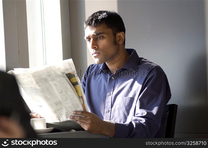 Young man reading a newspaper in a cafe.