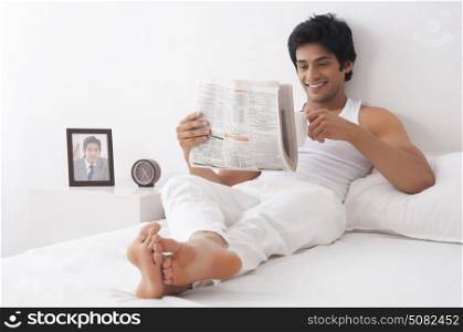 Young man reading newspaper in bed