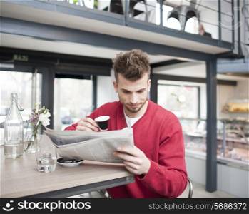 Young man reading newspaper while drinking coffee in cafe