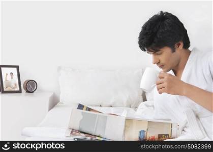 Young man reading newspaper while drinking tea