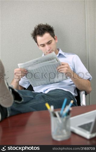 Young Man Reading Newspaper With Feet on Desk
