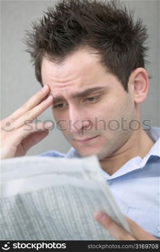Young Man Reading Newspaper With Hand to Brow