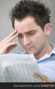 Young Man Reading Newspaper With Hand to Brow