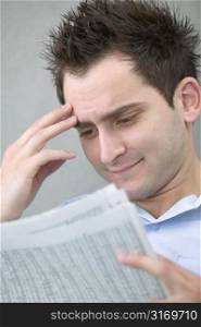 Young Man Reading Newspaper With Worried Smile