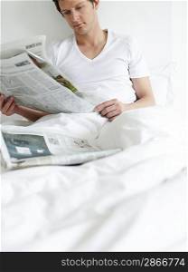 Young man reading newspapers in bed