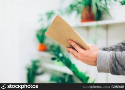 Young man reading open old paper book in the room with green plants, close up, vintage style. Spending time home during quarantine isolation. Education concept