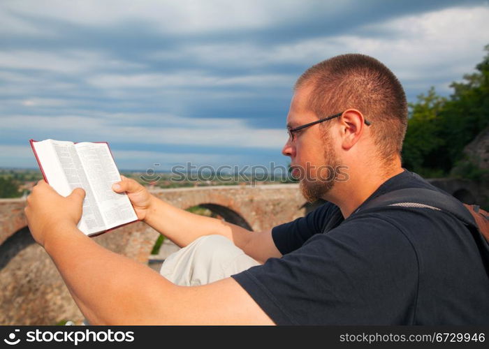 Young man reading the Bible sitting outdoors