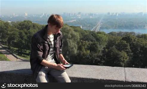 young man reads electronic book, on background nice view of capital city, Kiev Ukraine, then he leaves