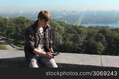 young man reads electronic book, on background nice view of capital city, Kiev Ukraine