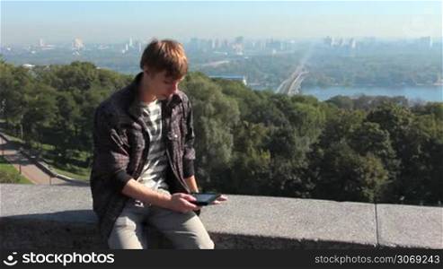 young man reads electronic book, on background nice view of capital city, Kiev Ukraine