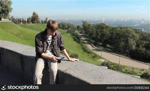 young man reads electronic book, on background nice wide view of capital city, Kiev Ukraine, then he leaves