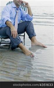 Young man relaxing on a lounge chair at the beach and talking on a mobile phone