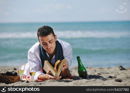 young man relaxing on beach at beautiful sunny day while reading book representing summer school and education concept