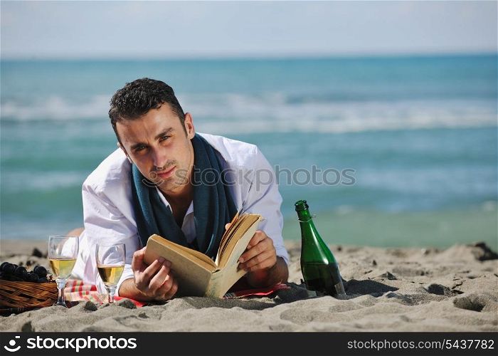 young man relaxing on beach at beautiful sunny day while reading book representing summer school and education concept