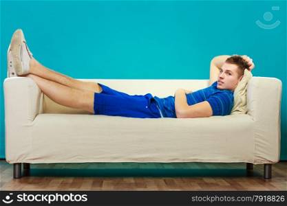 Young man relaxing on couch, teen pensive boy laying lazy on bed blue background