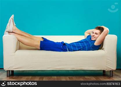 Young man relaxing on couch, teen positive boy laying lazy on bed blue background