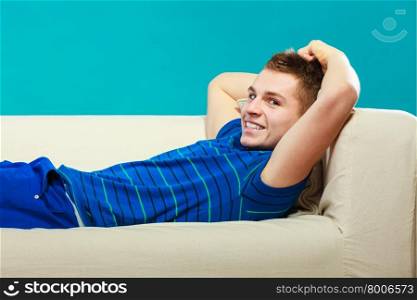 Young man relaxing on couch, teen positive boy laying lazy on bed blue background
