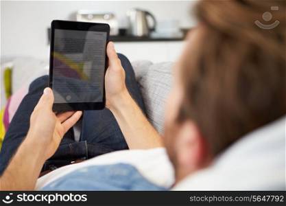 Young Man Relaxing On Sofa Using Digital Tablet