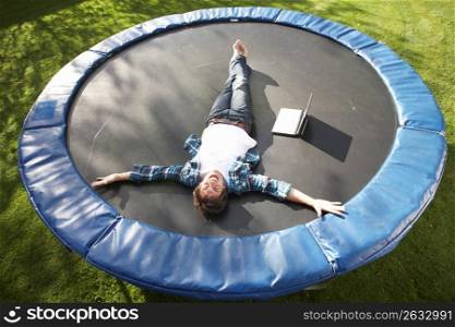 Young Man Relaxing On Trampoline With Laptop