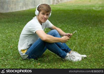 young man relaxing with a tablet pc listening music with headphones at the park, outdoor
