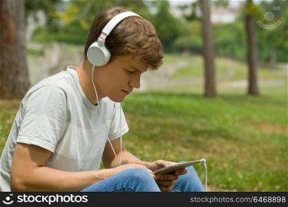 young man relaxing with a tablet pc listening music with headphones at the park, outdoor