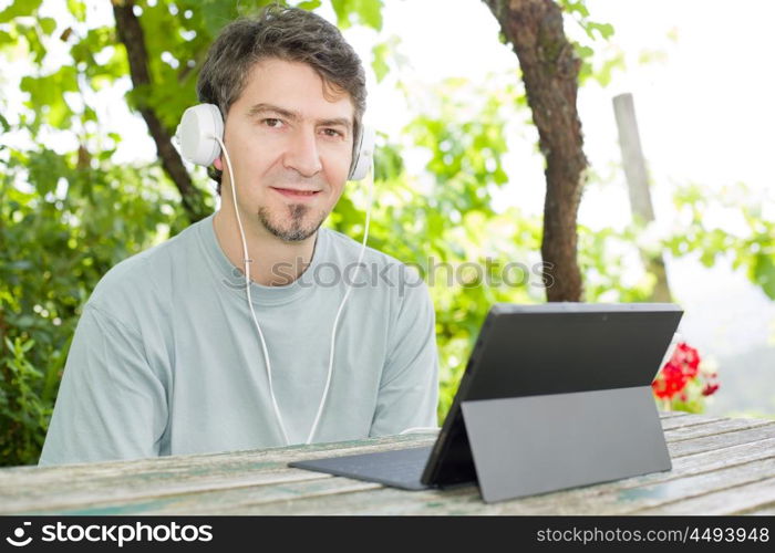 young man relaxing with a tablet pc listening music with headphones on a the park, outdoor