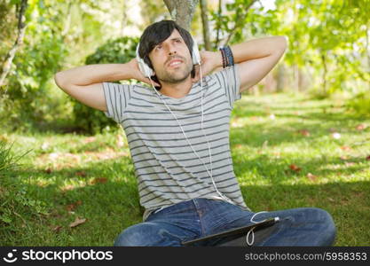 young man relaxing with a tablet pc listening music with headphones on a the park, outdoor