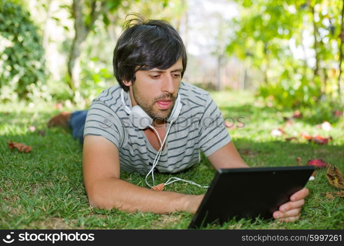 young man relaxing with a tablet pc listening music with headphones on a the park, outdoor